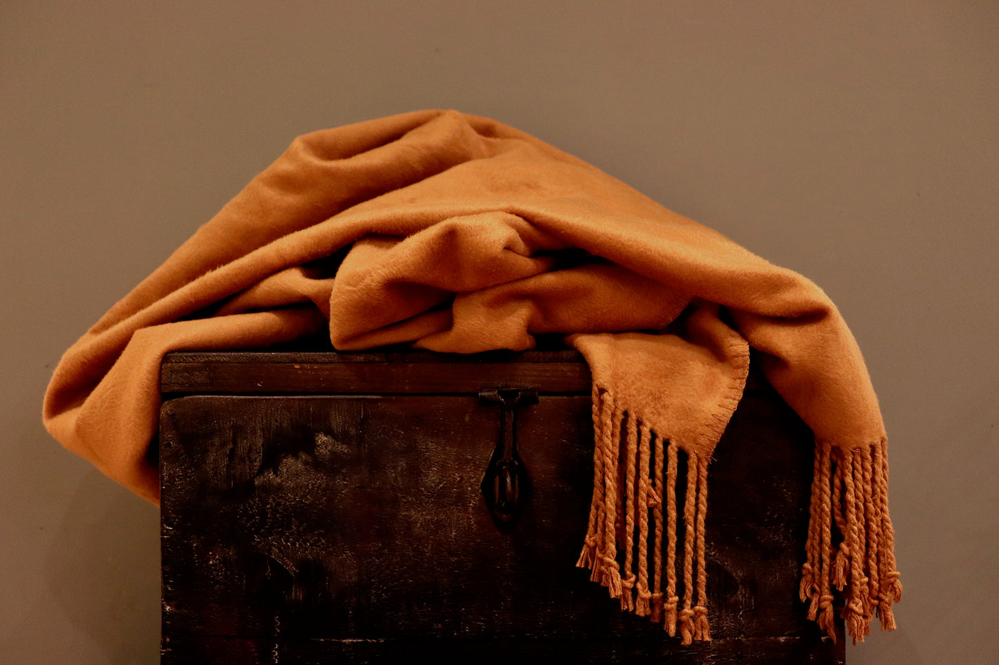 A burnt orange bamboo throw, incredibly soft, with tassels as a fringe, sitting on a wooden trunk.