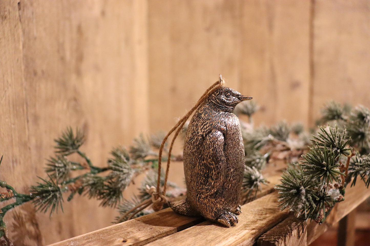 A penguin christmas tree ornament, in antique silver, hanging from a piece of string.