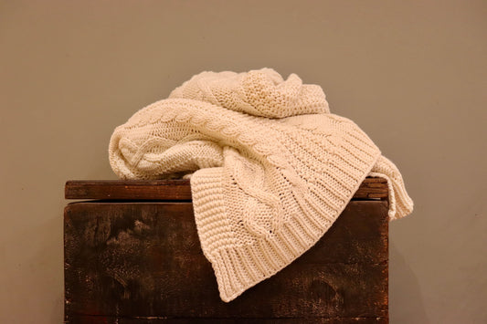Cream chunky knitted throw with a beautiful design, sitting on top of a dark wooden trunk.