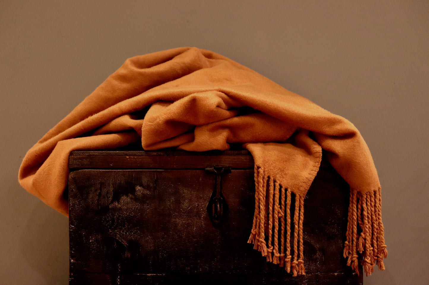 A burnt orange bamboo throw, incredibly soft, with tassels as a fringe, sitting on  a wooden trunk.