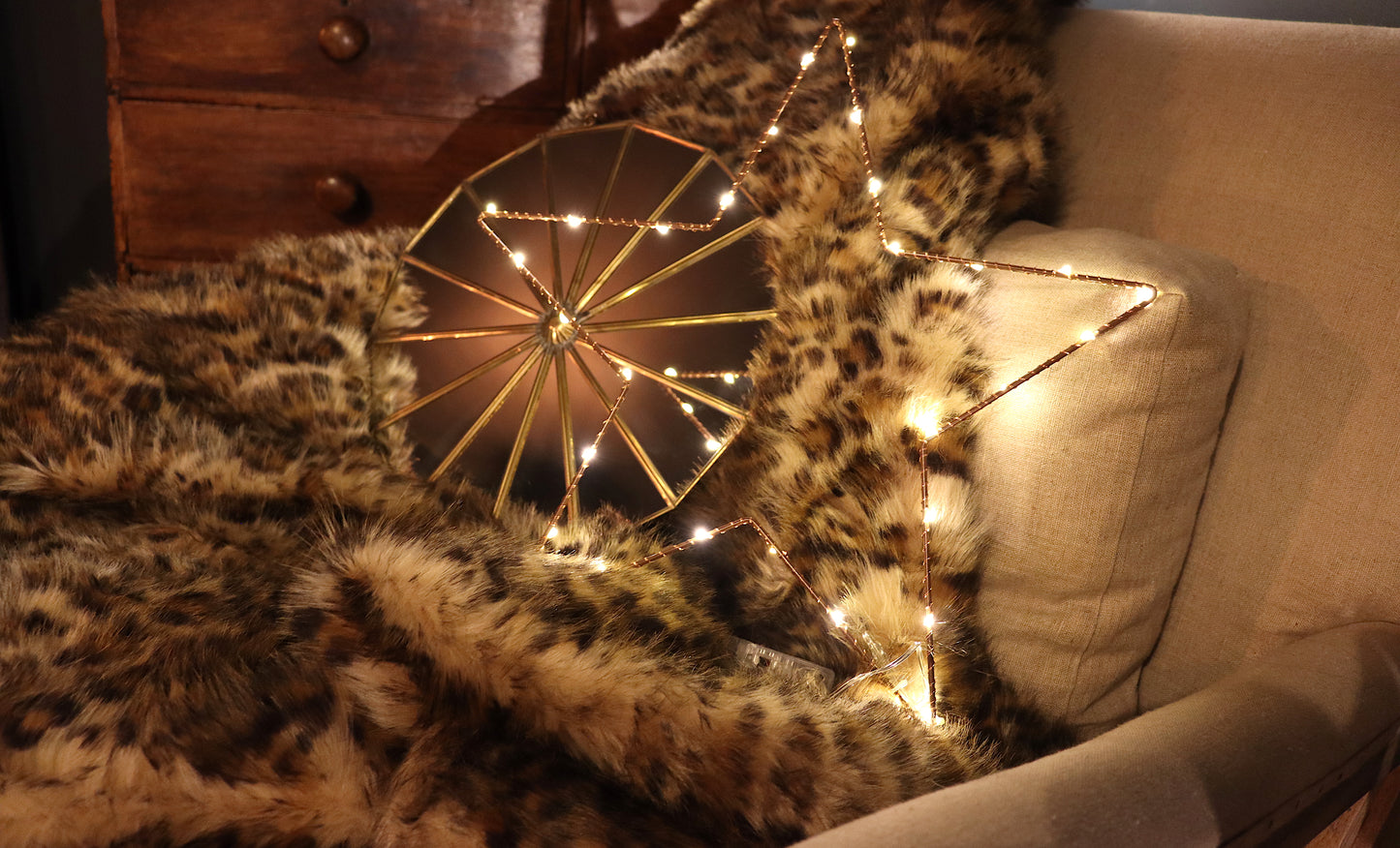Lit up battery powered wire star on a leopard print throw, and linen armchair with a brass decorative mirror. 