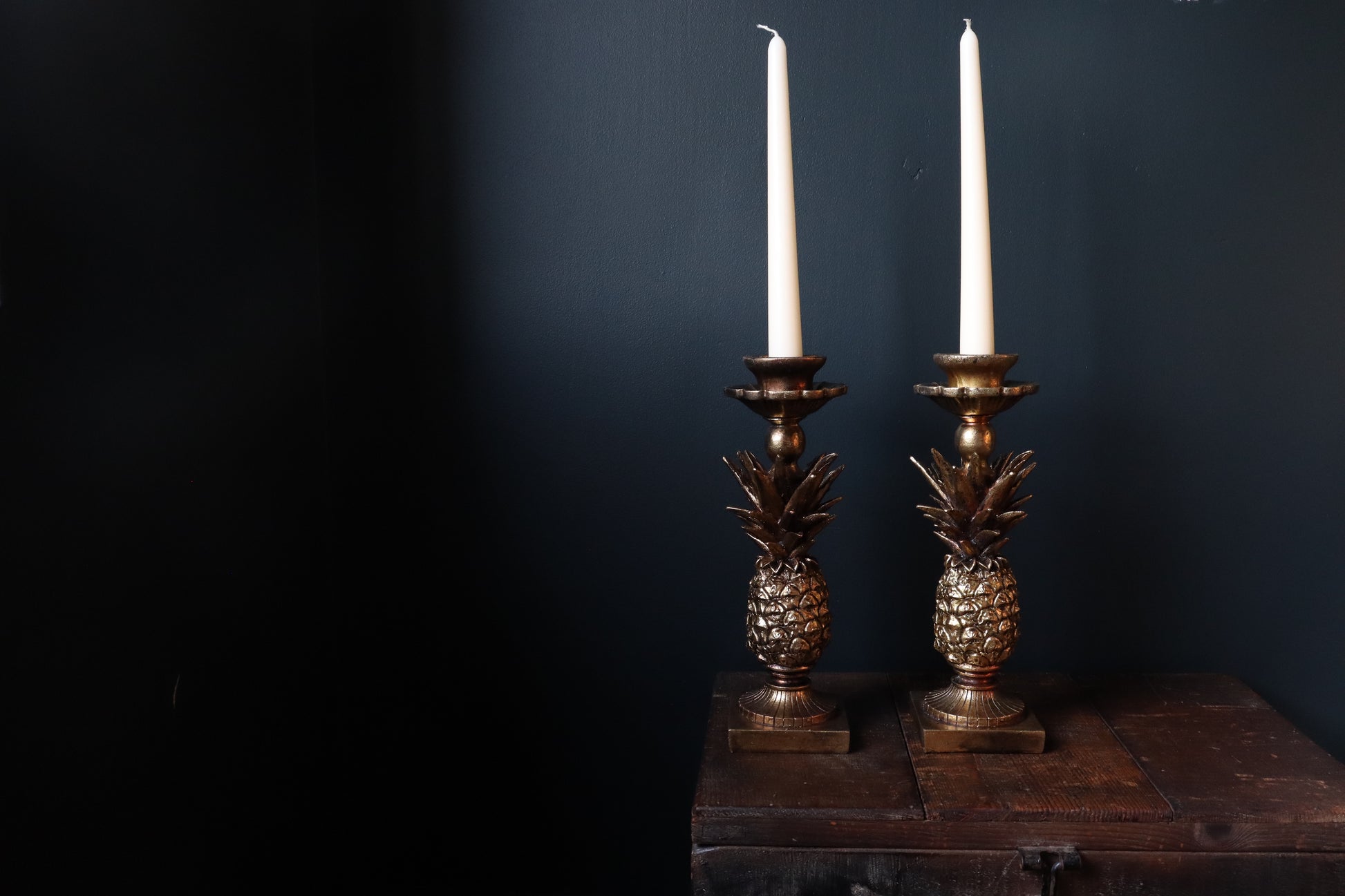 gold pineapple candle holder on a wooden surface with dark background holding 2 dinner candles