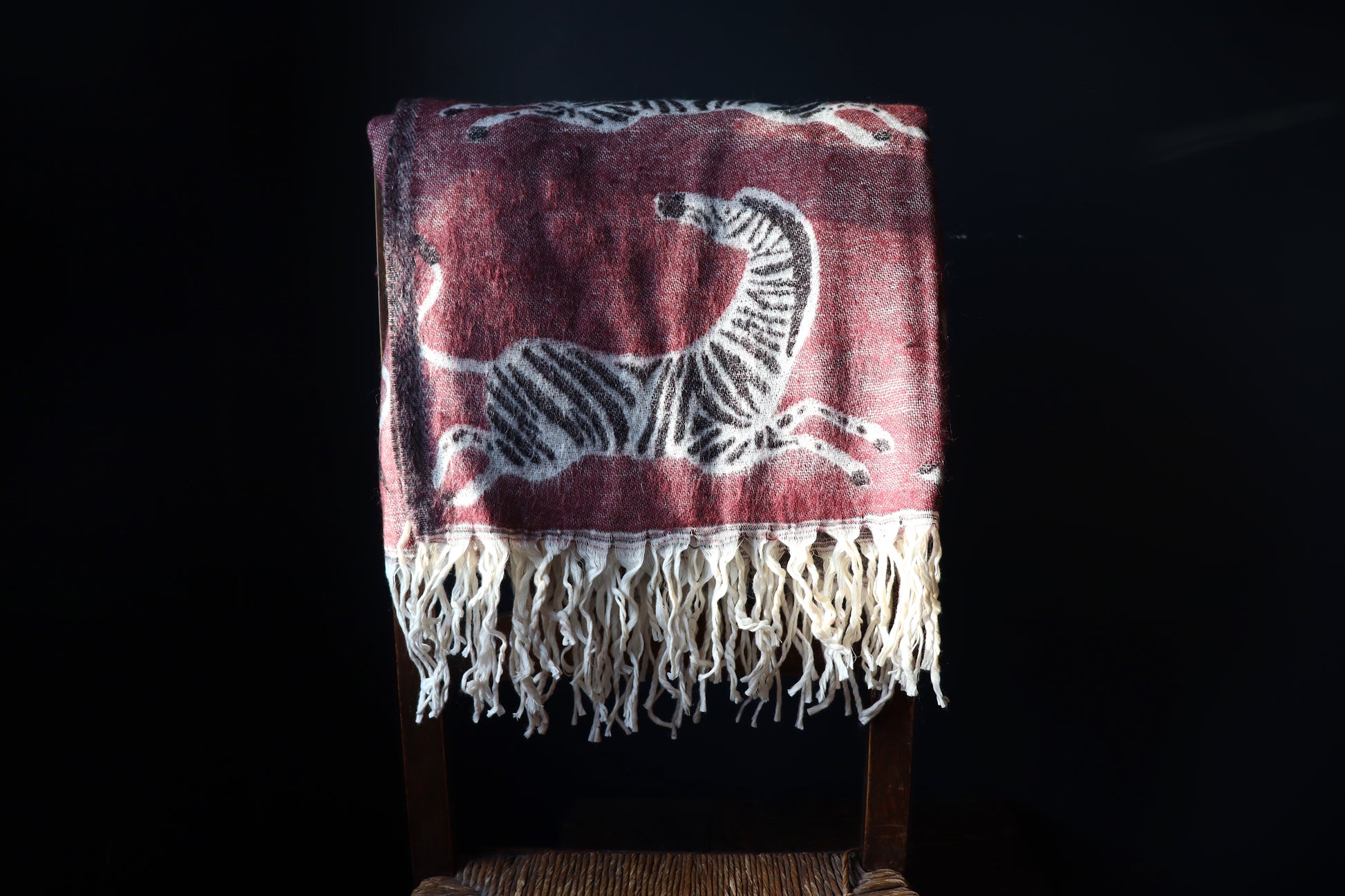 Wine coloured zebra throw on the back of a wooden chair with a dark background. 